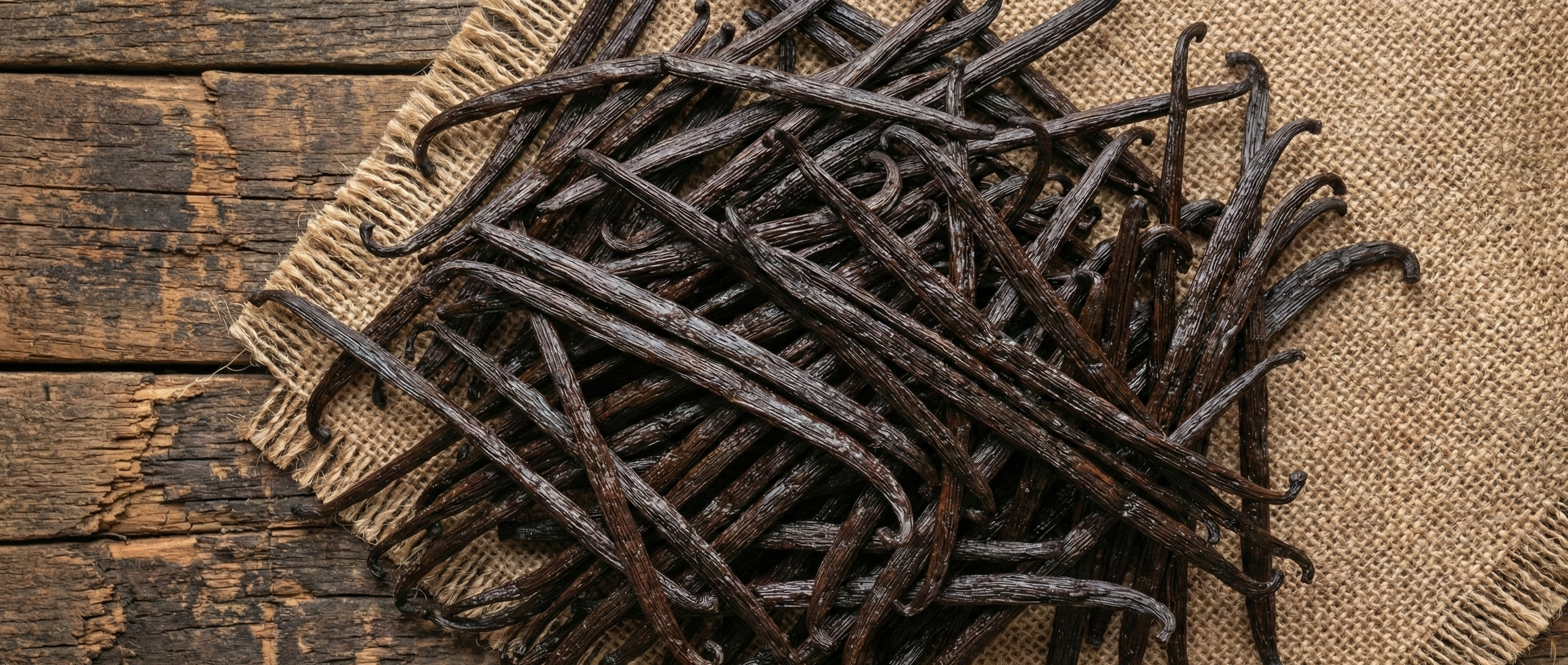 Gousses de vanille Bourbon de Madagascar en vrac présentées sur bois rustique et toile de jute naturelle